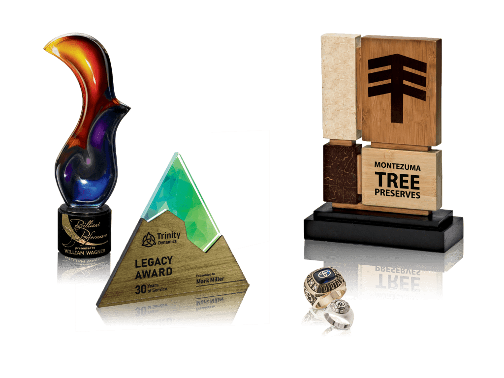a collection of custom employee recognition awards including a couple of glass awards, a wooden award, and two company rings.