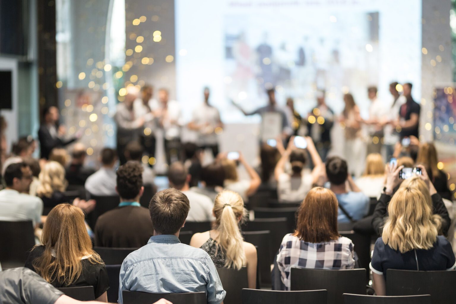 Young business team receiving award at best business project competition event. Business and entrepreneurship award ceremony theme. Focus on unrecognizable people in audience.