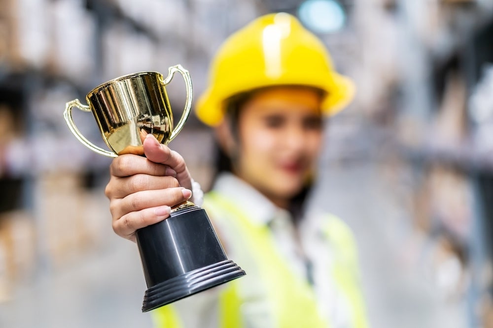 Happy woman warehouse worker holding a trophy after being selected as an outstanding employee, Selective focus of hand hold trophy